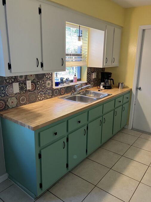 Completed kitchen refresh — sage green lower cabinets, white uppers, butcher block counters, tile backsplash