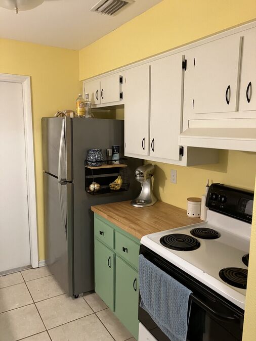 Kitchen fridge and stove side — green cabinets, white uppers, butcher block